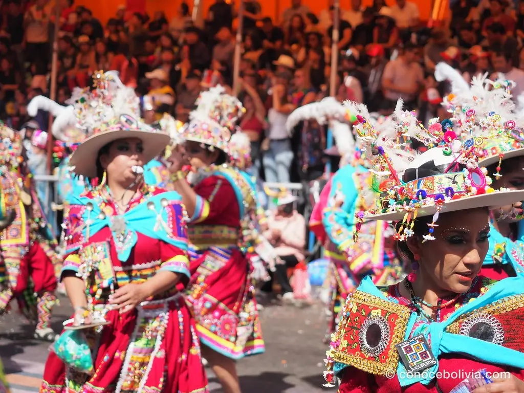 Bailarinas con sombreros cubiertos de cintas, flores y plumas, tocando silbatos durante el desfile