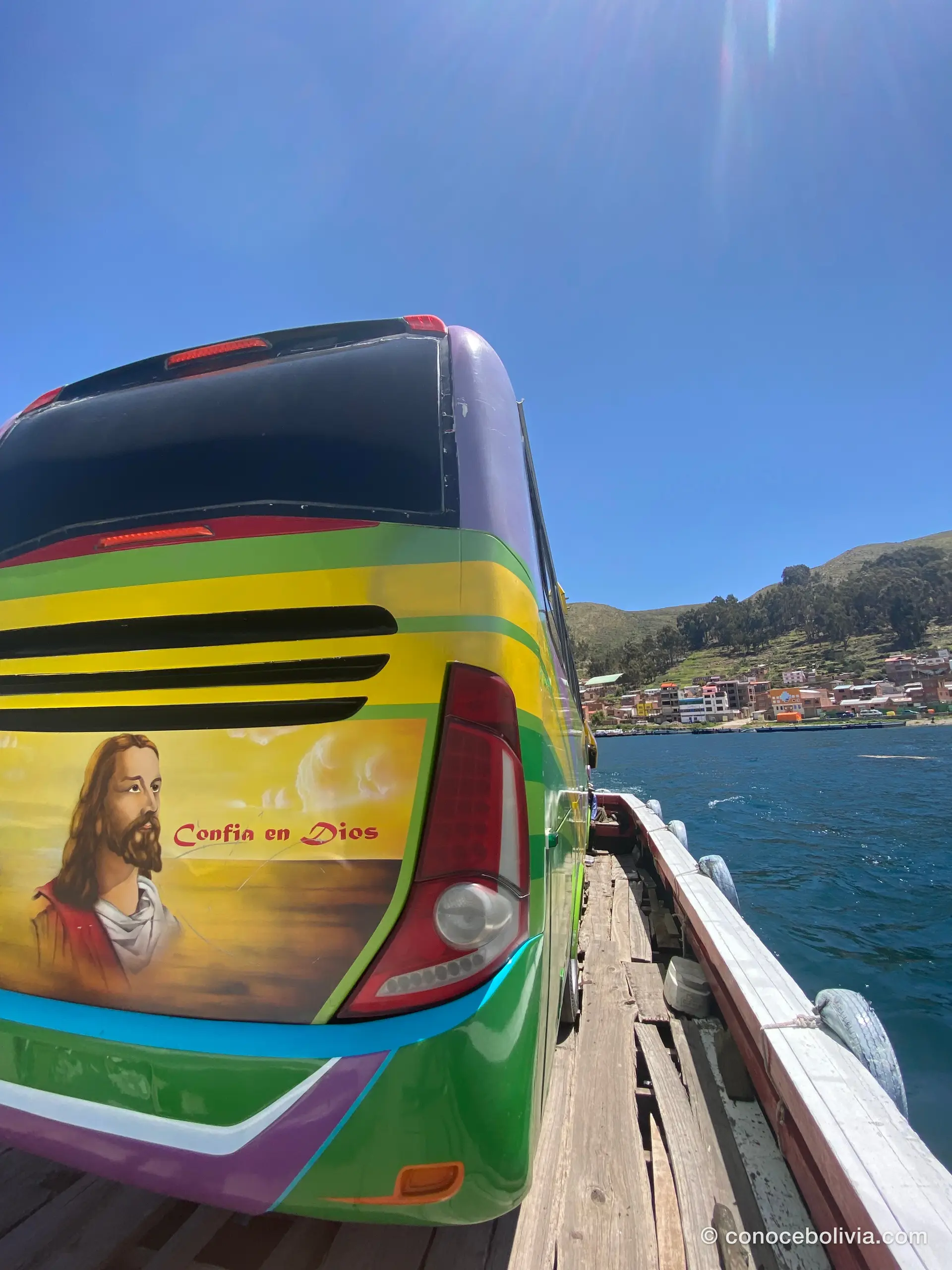 Bus pintado con la imagen de Jesús y el lema Confía en Dios, cruzando el Estrecho de Tiquina sobre una barcaza