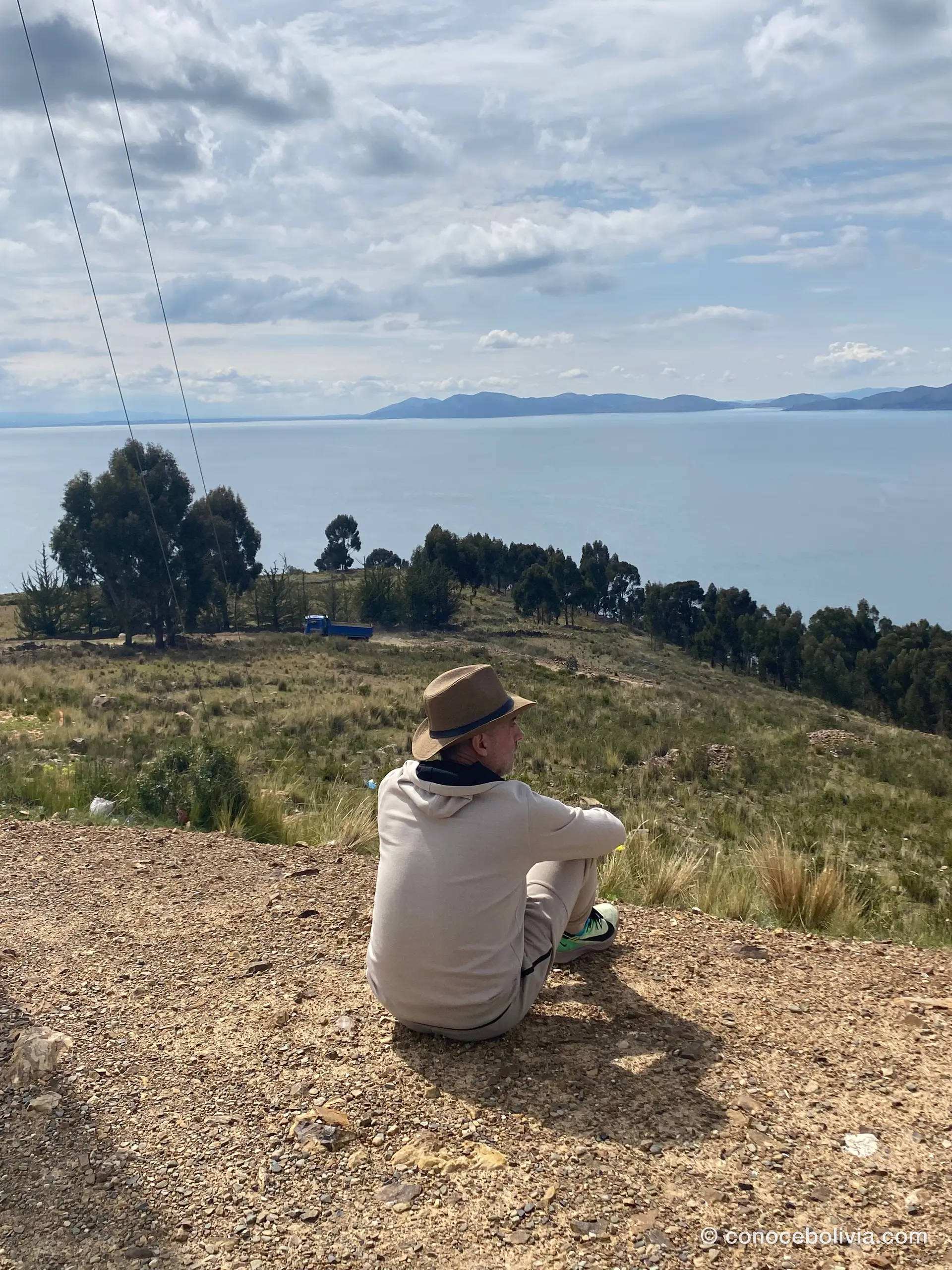Persona sentada mirando el Lago Titicaca desde una colina, con un camión al fondo