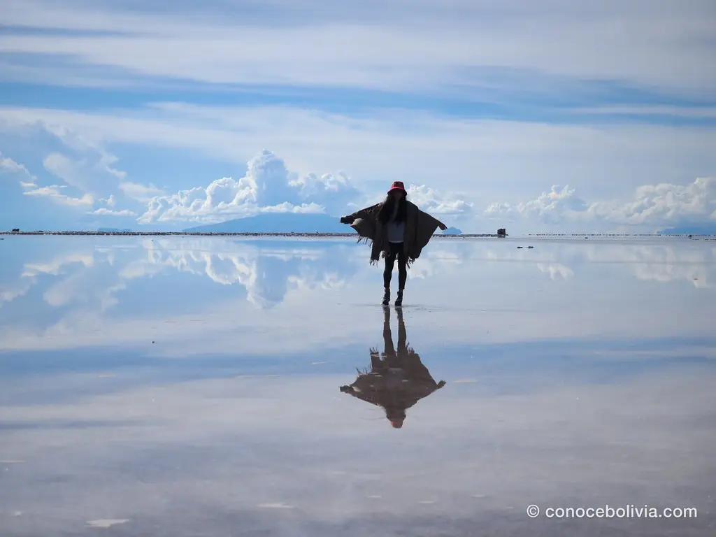 Persona con poncho al viento reflejada en el espejo de agua del Salar de Uyuni