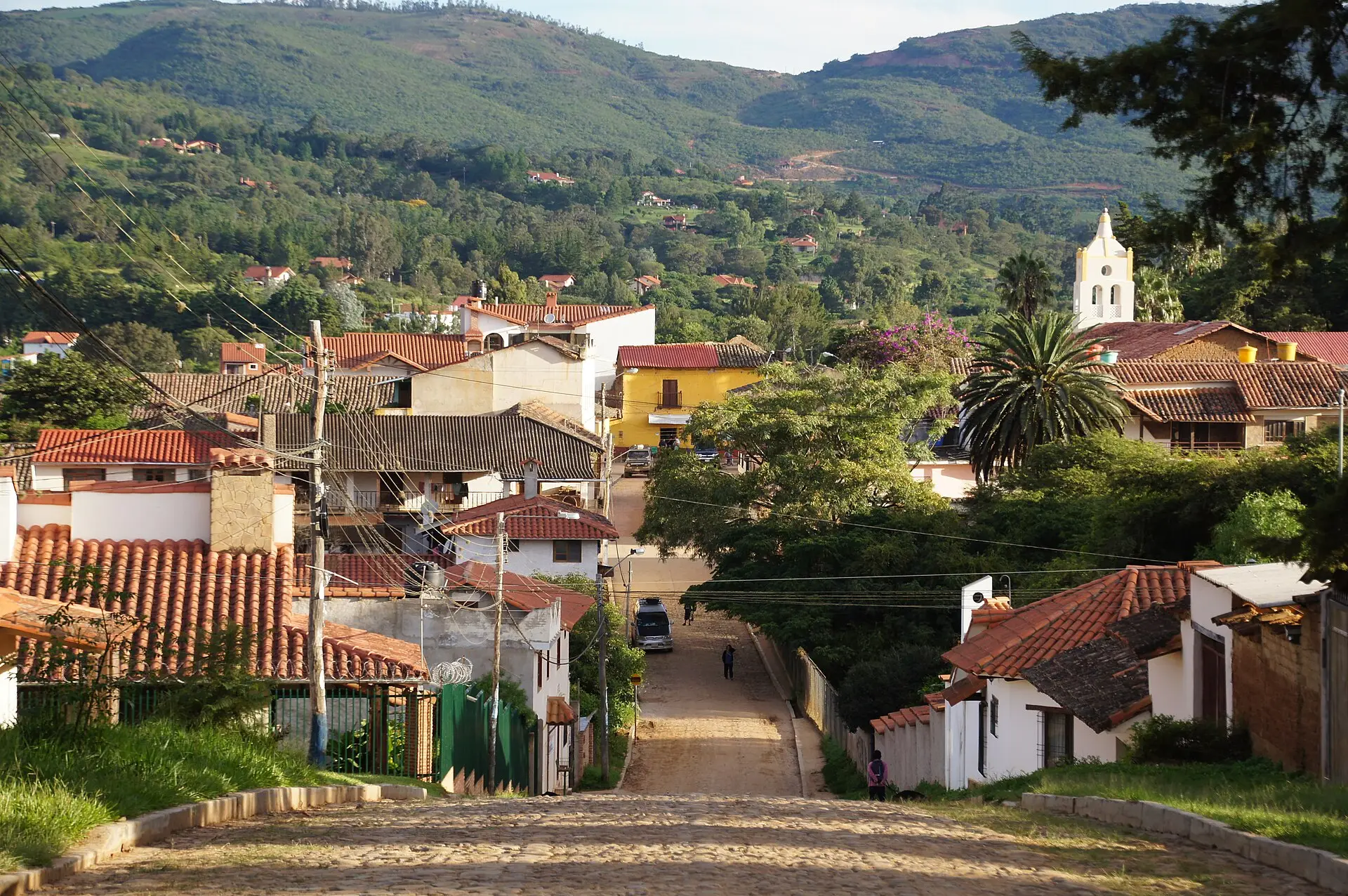 Calle empedrada de Samaipata bajando entre casas de tejas rojas, con la torre de la iglesia y los cerros al fondo